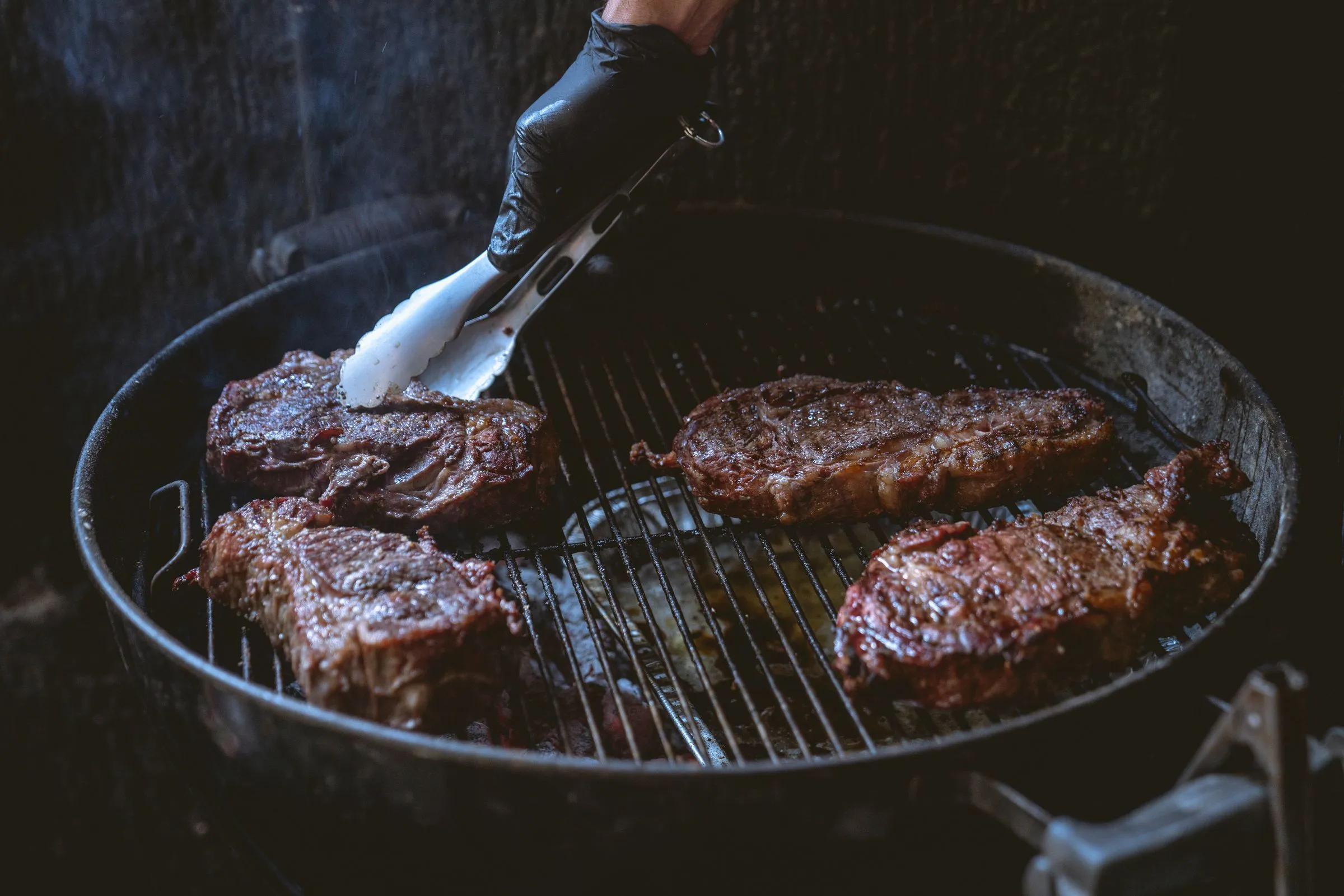 Carne a la brasa en parrilla redonda, manejada con pinzas por el parrillero